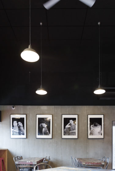 Comme à la maison Boutique à Annecy, boulangerie vue de détail sur les portraits noir et blanc sur un fond béton, plafond noir et luminaire acier, conçu par le studio frvr.