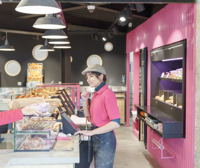 Comme à la maison boutique à Annecy, boulangerie vue sur vendeuse en uniforme, espace et meuble béton, acier et tôle rose, conçu par le studio frvr.
