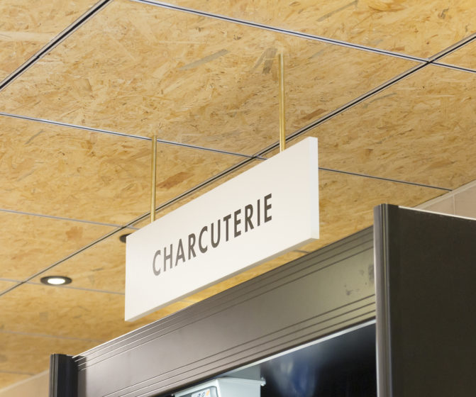 épicerie sur cours à Lyon, vue de détail sur la signalétique, plafond en bois triply, tube laiton, panneau blanc, texte noir, charcuterie. Conçu en collaboration, Pep's création et le studio frvr