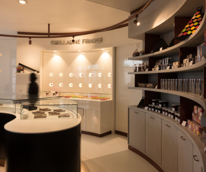 Pâtisserie Guillaume France à Lunel, vue générale avec vitrine centrale, mur à tablette chocolat, et étagère de produits sec confiture, biscuit, boutique conçue par l'agence de design frvr.