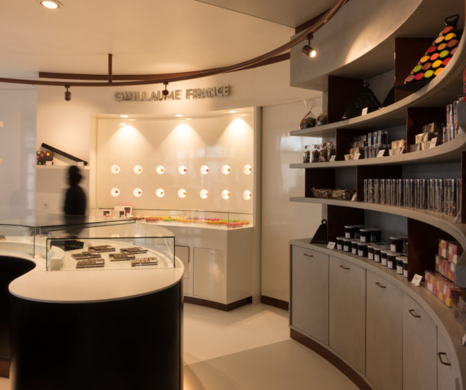 Pâtisserie Guillaume France à Lunel, vue générale avec vitrine centrale, mur à tablette chocolat, et étagère de produits sec confiture, biscuit, boutique conçue par l'agence de design frvr.