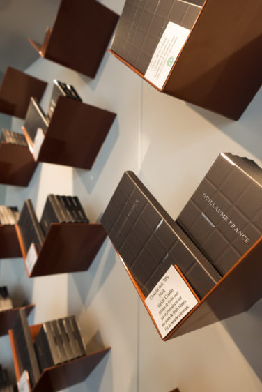 Pâtisserie Guillaume France à Lunel, vue en détail des tablettes de chocolat en libre service dans une structure en tôle acier laqué cuivre plié , boutique conçue par l'agence de design frvr.