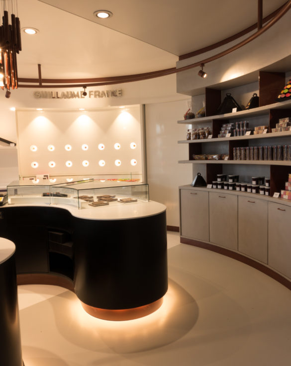 Pâtisserie Guillaume France à Lunel, détail du meuble revente stratifié gris et vue sur le mur macaron, boutique conçue par l'agence de design frvr.